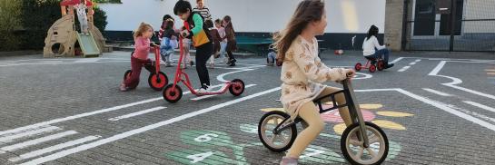 verschillende kinderen fietsen en steppen op een speelplaats en hebben samen plezier